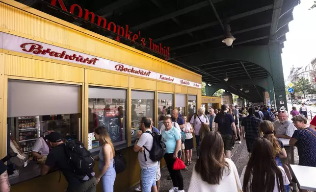 At Konnopke's Imbiss, a fast food restaurant under the tracks at Eberswalder Straße subway station, customers queue up for currywurst in a long line, in Berlin, Germany, Friday, May 24, 2024. The currywurst, Germany's sausage with curry sauce, promises to be among the most tantalizing gourmet treats on offer at the European Championship this summer. The currywurst is considered a fast-food delicacy in a country where the humble sausage enjoys great importance. (AP Photo/Markus Schreiber)