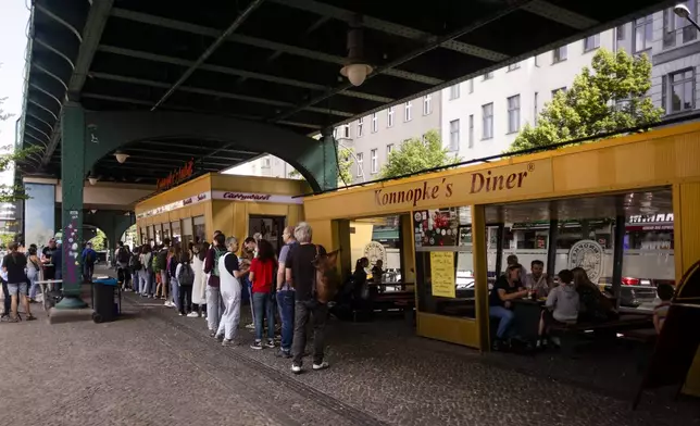 At Konnopke's Imbiss, a fast food restaurant under the tracks at Eberswalder Straße subway station, customers queue up for currywurst, in Berlin, Germany, Friday, May 24, 2024. The currywurst, Germany's sausage with curry sauce, promises to be among the most tantalizing gourmet treats on offer at the European Championship this summer. The currywurst is considered a fast-food delicacy in a country where the humble sausage enjoys great importance. (AP Photo/Markus Schreiber)