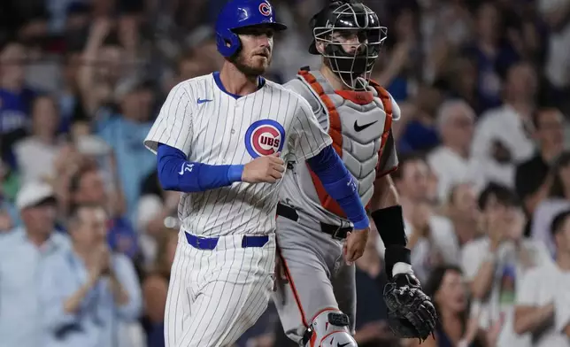 Chicago Cubs' Cody Bellinger, left, scores next to San Francisco Giants catcher Curt Casali during the eighth inning of a baseball game in Chicago, Tuesday, June 18, 2024. (AP Photo/Nam Y. Huh)