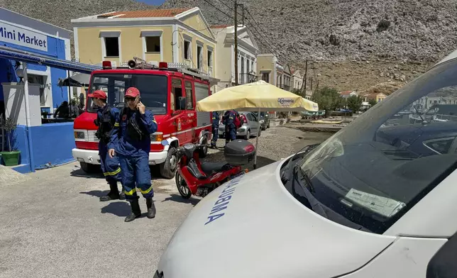 Greek Fire brigade personnel walk on a beachfront of Symi island, Greece Sunday, June 9, 2024. Police said that a body believed to be that of missing British TV presenter Michael Mosley was found on a Greek island Sunday morning. (AP Photo/Antonis Mystiloglou)