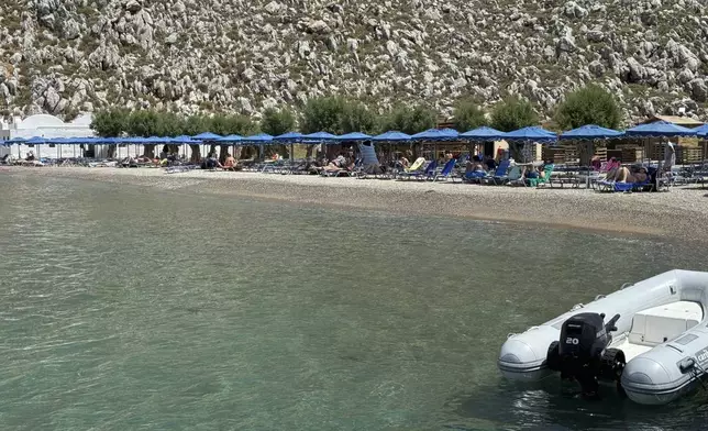 People sit on the beach of Agios Nikolaos from where British doctor and television presenter Michael Mosley, is believed to have set out, on the southeastern Aegean Sea island of Symi, Greece, Friday, June 7, 2024. Greek police say an ongoing major search and rescue operation on the small eastern Aegean island of Symi has still not located British doctor and television presenter Michael Mosley, who went missing on Wednesday afternoon after reportedly going for a walk. (AP Photo/Antonis Mystiloglou)