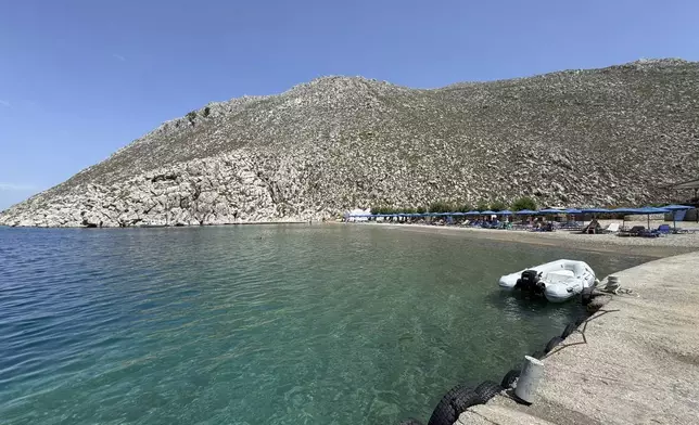 People sit on the beach of Agios Nikolaos from where British doctor and television presenter Michael Mosley, is believed to have set out, on the southeastern Aegean Sea island of Symi, Greece, Friday, June 7, 2024. Greek police say an ongoing major search and rescue operation on the small eastern Aegean island of Symi has still not located British doctor and television presenter Michael Mosley, who went missing on Wednesday afternoon after reportedly going for a walk. (AP Photo/Antonis Mystiloglou)