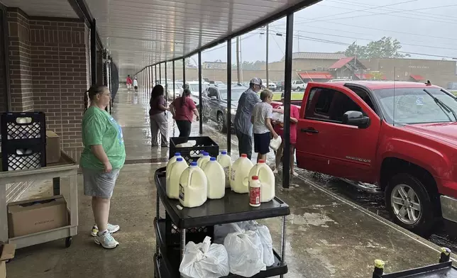 Volunteers hand out bags of groceries and jugs of milk to cars lined up at Fordyce High School in Fordyce, Ark., Wednesday, June 26, 2024. The school is one of several food distribution sites that have been set up to help residents after a mass shooting at the Mad Butcher grocery store. (AP Photo/Andrew DeMillo)