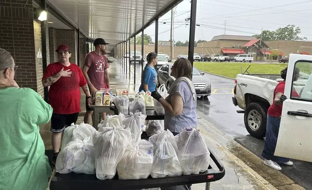Volunteers hand out bags of groceries and jugs of milk to cars lined up at Fordyce High School in Fordyce, Arkansas on Wednesday, June 26, 2024. The school is one of several food distribution sites that have been set up to help residents after a mass shooting at the Mad Butcher grocery store. (AP Photo/Andrew DeMillo)