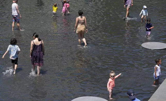 Families wade in ankle deep water at Yards Park Canal Basin, Sunday, June 16, 2024, as temperatures begin to steam up in Washington. The park usually has a waterfall feature which is currently down for maintenance. (AP Photo/Jacquelyn Martin)