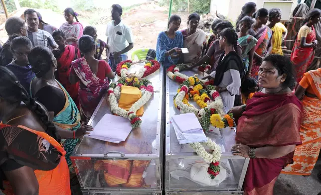 Relatives of a married couple, who died after drinking illegally brewed liquor, stand next to the caskets containing their bodies, in Kallakurichi district of the southern Indian state of Tamil Nadu, India, Thursday, June 20, 2024. The state's chief minister M K Stalin said the 34 died after consuming liquor that was tainted with methanol, according to the Press Trust of India news agency. (AP Photo/R. Parthibhan)