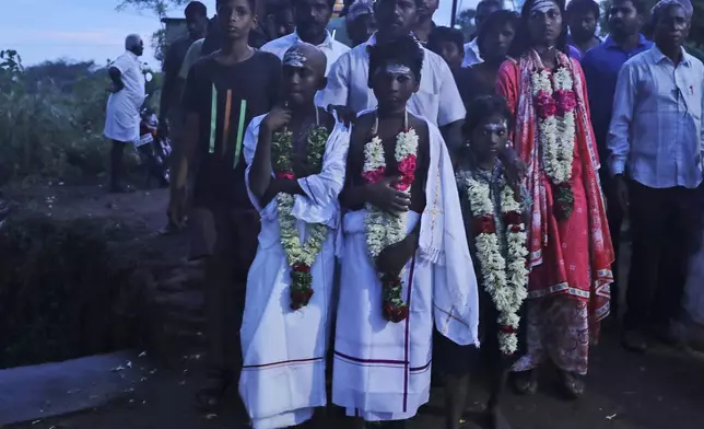 Children wear ceremonial clothes as they wait for the cremation of their parents, both of whom died after drinking illegally brewed liquor, in Kallakurichi district of the southern Indian state of Tamil Nadu, India, Thursday, June 20, 2024. The state's chief minister M K Stalin said the 34 died after consuming liquor that was tainted with methanol, according to the Press Trust of India news agency. (AP Photo/R. Parthibhan)