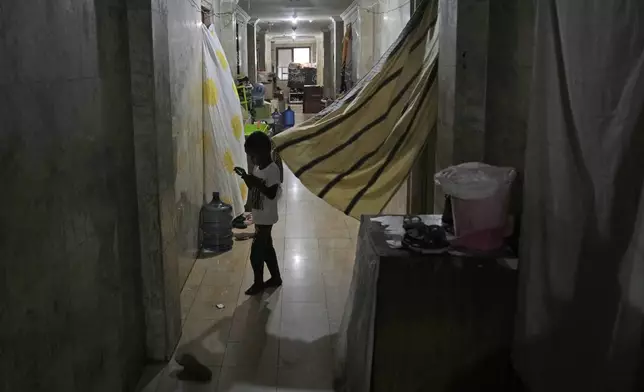 A child plays with a mobile phone in the hallway of Hotel Kolekta, turned into a shelter for refugees, in Batam, an island in northwestern Indonesia, Thursday, May 16, 2024. The former tourist hotel was converted in 2015 into a temporary shelter that today houses 228 refugees from conflict-torn nations including Afghanistan, Somalia, Sudan and elsewhere. (AP Photo/Dita Alangkara)