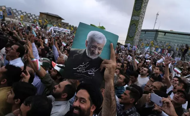 A cleric holds up a poster of Saeed Jalili, a candidate for the June 28, presidential election, during his campaign rally in Tehran, Iran, Monday, June 24, 2024. (AP Photo/Vahid Salemi)