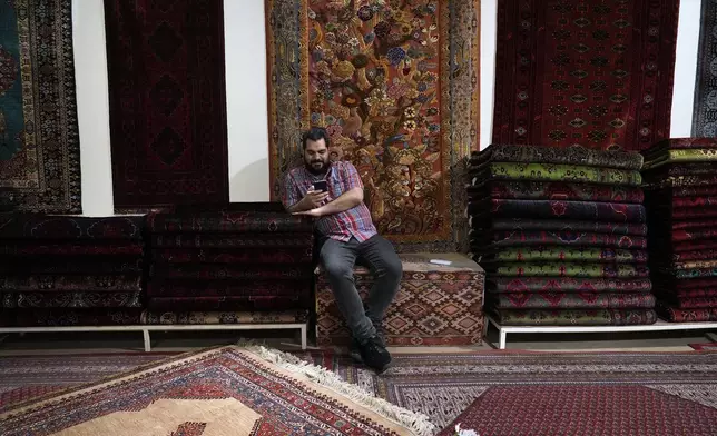 A salesman works on his cell phone at a carpet shop in the old main bazaar of Tehran, Iran, Thursday, June 13, 2024. The rise of the “Hamster Kombat” app in Iran highlights a harsher truth facing the Islamic Republic's economy ahead of its presidential election this week to replace the late President Ebrahim Raisi, who died in a helicopter crash in May. (AP Photo/Vahid Salemi)