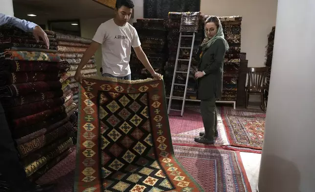 A shopkeeper shows a kilim to a customer at a carpet shop in the old main bazaar of Tehran, Iran, Thursday, June 13, 2024. The rise of the “Hamster Kombat” app in Iran highlights a harsher truth facing the Islamic Republic's economy ahead of its presidential election this week to replace the late President Ebrahim Raisi, who died in a helicopter crash in May. (AP Photo/Vahid Salemi)