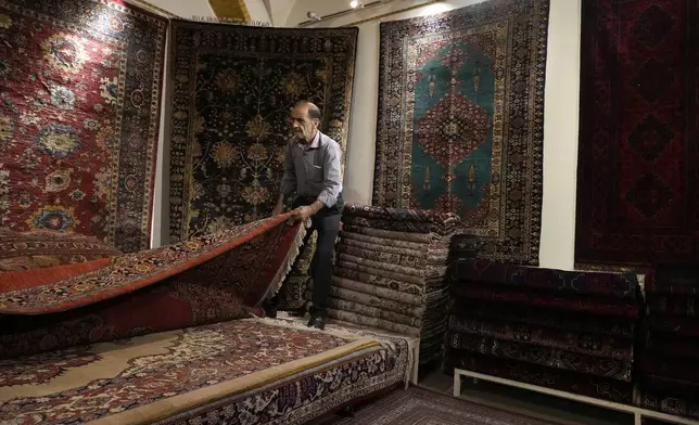A shopkeeper shows a carpet to a customer at a carpet shop in the old main bazaar of Tehran, Iran, Thursday, June 13, 2024. The rise of the “Hamster Kombat” app in Iran highlights a harsher truth facing the Islamic Republic's economy ahead of its presidential election this week to replace the late President Ebrahim Raisi, who died in a helicopter crash in May. (AP Photo/Vahid Salemi)