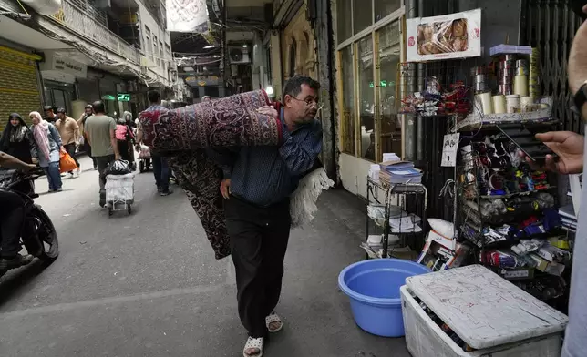 A man carries a carpet in the old main bazaar of Tehran, Iran, Thursday, June 13, 2024. The rise of the “Hamster Kombat” app in Iran highlights a harsher truth facing the Islamic Republic's economy ahead of its presidential election this week to replace the late President Ebrahim Raisi, who died in a helicopter crash in May. (AP Photo/Vahid Salemi)