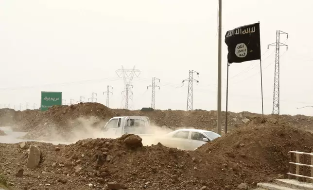 FILE - Islamic State militants pass a checkpoint bearing the group's trademark black flag in the village of Maryam Begg in Kirkuk, 290 kilometers (180 miles) north of Baghdad, Iraq, Sept. 29, 2014. Ten years after the Islamic State group declared its caliphate in large parts of Iraq and Syria, the extremists now control no land, have lost many prominent founding leaders and are mostly away from the world news headlines. (AP Photo/Hadi Mizban, File)