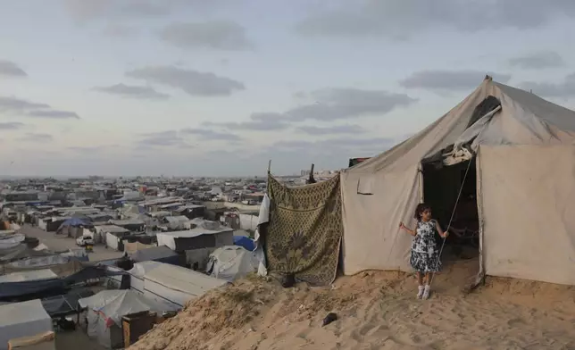 A Palestinian girl stands at the entrance of her family tent at a makeshift tent camp for those displaced by the Israeli air and ground offensive on the Gaza Strip in Khan Younis, Gaza, Tuesday, June 18, 2024. (AP Photo/Jehad Alshrafi)