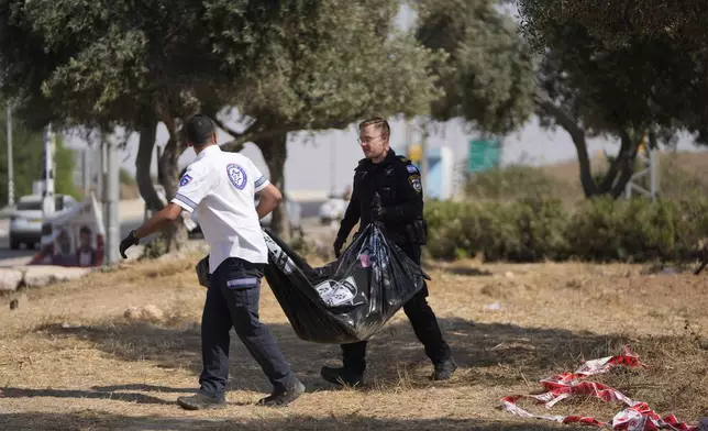 An Israeli Police officer and paramedic remove a body found at the Sha'ar HaNegev junction in southern Israel, Thursday, June 13, 2024, an area besieged by a cross-border attack by Hamas militants on Oct. 7, 2023. Israeli Police say that the body, found alongside a combat vest and a shirt with Arabic writing, will be sent for forensic investigation. (AP Photo/Ohad Zwigenberg)