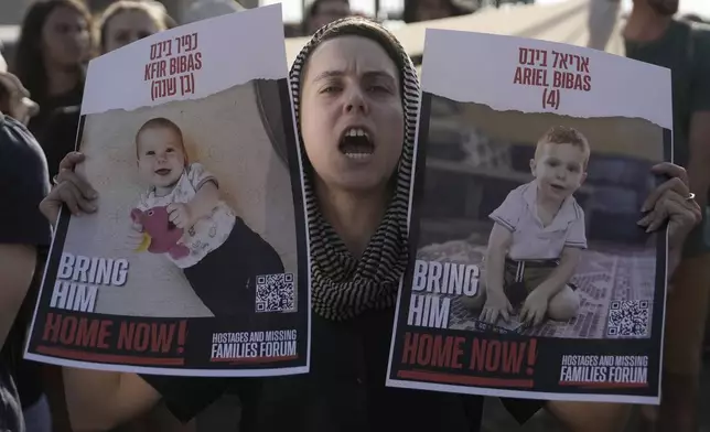 A woman holds posters of Kfir and Ariel Bibas, who are in Hamas captivity with their parents in the Gaza Strip, as students march towards The Knesset, Israel's parliament, to call for a deal to release hostages, in Jerusalem, Thursday, June 13, 2024. (AP Photo/Mahmoud Illean)