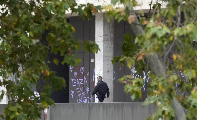 A police officer walks past a wall left with graffiti by pro-Palestinian protesters at the California State University, Los Angeles, Thursday, June 13, 2024. A takeover of a building at California State University, Los Angeles, by demonstrators protesting Israel's war against Hamas in Gaza ended early Thursday, leaving the facility trashed and covered with graffiti. (AP Photo/Damian Dovarganes)