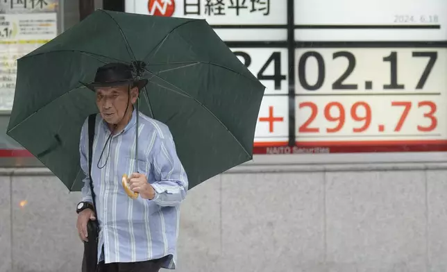 A person walks in the rain in front of an electronic stock board showing Japan's Nikkei 225 index at a securities firm Tuesday, June 18, 2024, in Tokyo. Shares were mostly higher in Asia on Tuesday after U.S. stocks rallied to more records, with gains for technology companies pushing the benchmarks higher. (AP Photo/Eugene Hoshiko)