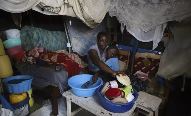 Jacinter Awino, 33, holds her son as she cleans utensils in the Kibera slum of the capital Nairobi, Kenya, Tuesday, May 28, 2024. Jacinter shares a small tin house with her husband and four children. The 33-year-old housewife and her mason husband are unable to raise the $3,800 purchase price for a one-room government house. Their tin one was constructed for $380 and lacks a toilet and running water. (AP Photo/Andrew Kasuku)