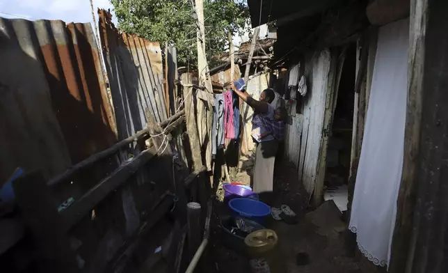 Jacinter Awino, 33, carries her son as she does laundry in the Kibera slum of the capital Nairobi, Kenya, Tuesday, May 28, 2024. Jacinter shares a small tin house with her husband and four children. The 33-year-old housewife and her mason husband are unable to raise the $3,800 purchase price for a one-room government house. Their tin one was constructed for $380 and lacks a toilet and running water. (AP Photo/Andrew Kasuku)