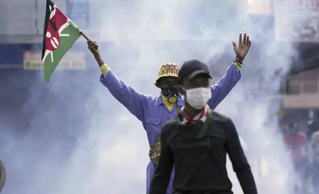 An anti-government protester waves a Kenyan flag as police fire tear gas at them during a protest over proposed tax hikes in a finance bill in downtown Nairobi, Kenya Tuesday, June. 25, 2024. (AP Photo/Brian Inganga)