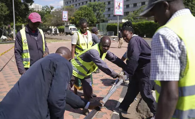 Nairobi county workers repair a road barrier in downtown Nairobi, Kenya, Wednesday, June 26, 2024. Thousands of protesters stormed and burned a section of Kenya's parliament Tuesday to protest tax proposals. Police responded with gunfire and several protesters were killed. (AP Photo/Brian Inganga)