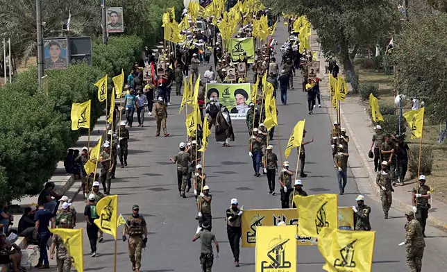 FILE - Iraqi Popular Mobilization Forces march as they hold their flag and posters of Iraqi and Iranian Shiites spiritual leaders during "al-Quds" or Jerusalem Day, in Baghdad, Iraq, June 8, 2018. Thousands of fighters from Iran-backed groups in the Middle East are offering to come to Lebanon to join the militant Hezbollah group in its fight with Israel. (AP Photo/Hadi Mizban, File)