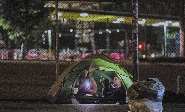 People sit inside a tent set on a sidewalk near City Hall downtown Los Angeles early morning Wednesday, June 26, 2024. The number of homeless residents counted in Los Angeles County has dipped slightly, decreasing by about 0.3% since last year as California continues to struggle with the long-running crisis of tens of thousands of people sleeping in cars and encampments. (AP Photo/Damian Dovarganes)