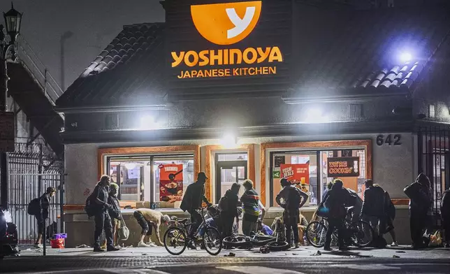 People linger outside a Yoshinoya restaurant across McArthur Park early morning Wednesday, June 26, 2024. The number of homeless residents counted in Los Angeles County has dipped slightly, decreasing by about 0.3% since last year as California continues to struggle with the long-running crisis of tens of thousands of people sleeping in cars and encampments. (AP Photo/Damian Dovarganes)