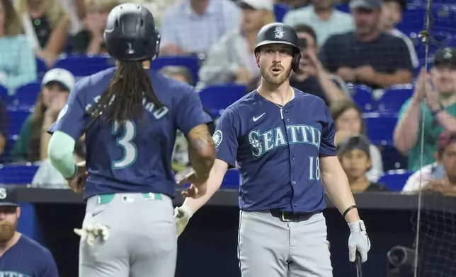 Seattle Mariners' J.P. Crawford (3) is congratulated by Mitch Garver (18) after Crawford scored on a wild pitch during the first inning of a baseball game against the Miami Marlins, Saturday, June 22, 2024, in Miami. (AP Photo/Wilfredo Lee)