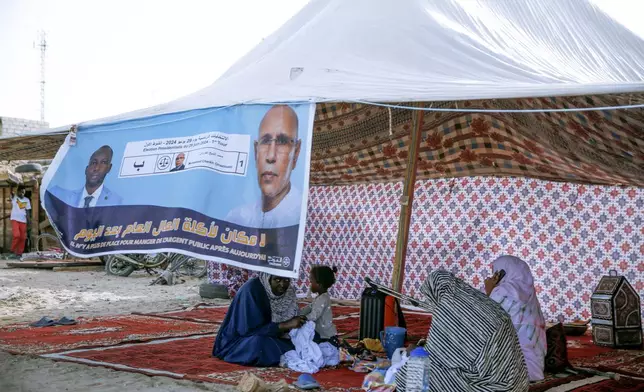 Women sit behind an electoral banner for Mauritanian president Mohamed Ould Ghazouani, during a campaign rally ahead of the presidential elections in Nouakchott, Mauritania, Wednesday, June 26, 2024. The banner reads: "There is no place for people embezzling public funds anymore." (AP Photo/Mamsy Elkeihel)