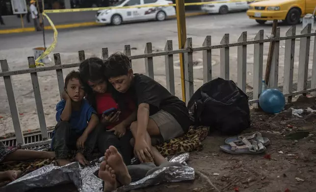 The Bolaños children, from Venezuela, watch videos on a mobile phone outside the bus terminal where they are living with their single mother Keilly and one other sibling, along with other migrants in Villahermosa, Mexico, Saturday, June 8, 2024. Their mother was captured in the northern state of Juarez, where she said she was beaten by the military in front of her children, loaded on a bus for two days, and left in Villahermosa. (AP Photo/Felix Marquez)