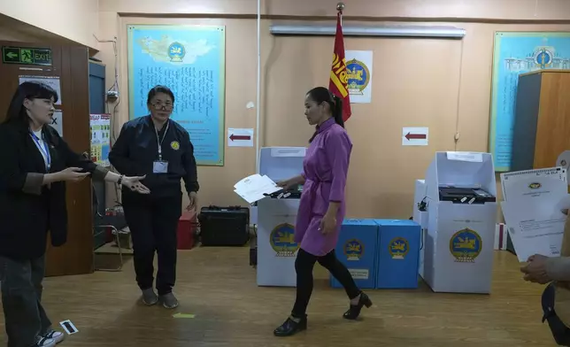 A voter hands over a folder as she leaves after casting her vote into a counting machine at a polling station in the Ger District on the outskirts of Ulaanbaatar, Mongolia, Friday, June 28, 2024. Voters in Mongolia are electing a new parliament on Friday in their landlocked democracy that is squeezed between China and Russia, two much larger authoritarian states. (AP Photo/Ng Han Guan)