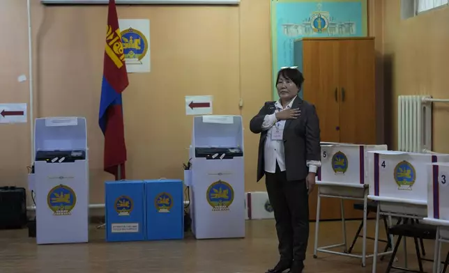 A electoral worker holds her hand to her chest as the national anthem is played before polling starts at a polling station in Ulaanbaatar, Mongolia, Friday, June 28, 2024. Voters in Mongolia are electing a new parliament on Friday in their landlocked democracy that is squeezed between China and Russia, two much larger authoritarian states. (AP Photo/Ng Han Guan)