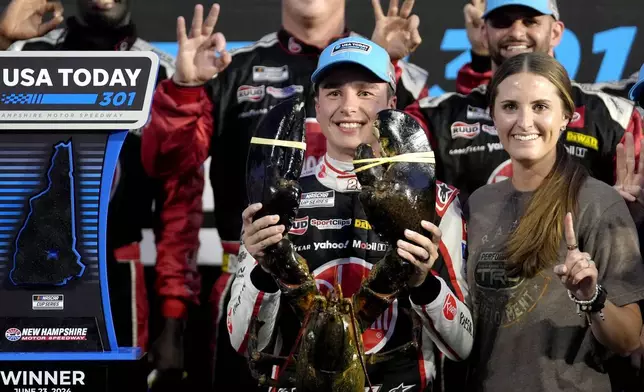 Christopher Bell, front left, holds up a lobster while standing with his wife Morgan, front right, as they celebrate after he won the NASCAR Cup Series race at New Hampshire Motor Speedway, Sunday, June 23, 2024, in Loudon, N.H. (AP Photo/Steven Senne)