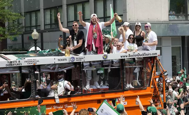 Boston Celtics' Kristaps Porzingis, center wearing the Celtics medallion, gestures to fans along the NBA championship team's duck boat parade Friday, June 21, 2024, in Boston. (AP Photo/Michael Dwyer)