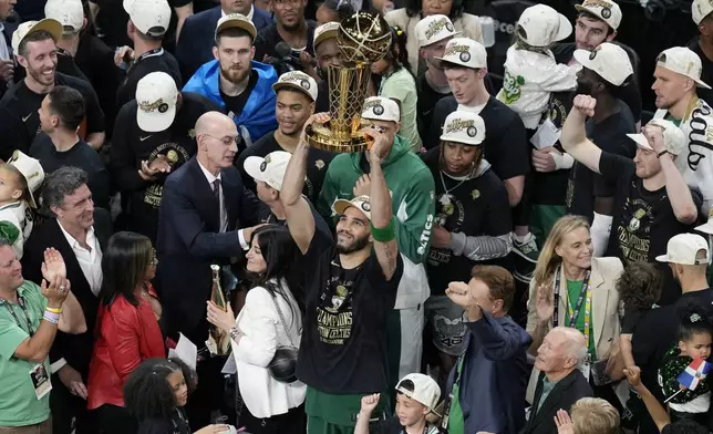 Boston Celtics' Jayson Tatum, center, raises the trophy after defeating the Dallas Mavericks in Game 5 of the NBA basketball finals, Monday, June 17, 2024, in Boston. (AP Photo/Michael Dwyer)