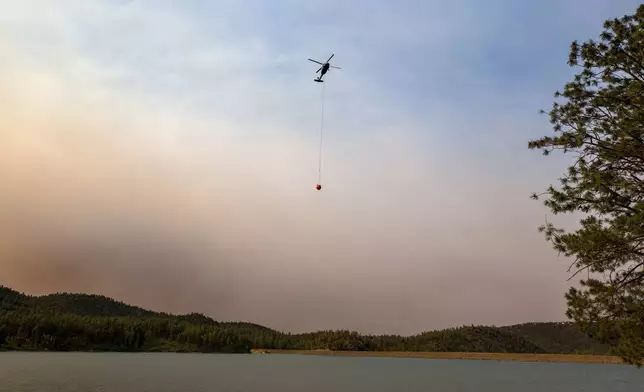 A helicopter collects water from Mescalero lake near the Inn of the Mountain Gods Resort in Ruidoso, N.M., as authorities fight wildfires Tuesday, June 18, 2024. Thousands of residents fled their homes as a wildfire swept into the mountain village of Ruidoso in southern New Mexico. (AP Photo/Andres Leighton)