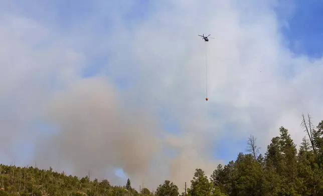 A helicopter flies over a wildfire in Ruidoso, N.M., Tuesday, June 18, 2024. Thousands of residents fled their homes as a wildfire swept into the mountain village of Ruidoso in southern New Mexico. (AP Photo/Andres Leighton)