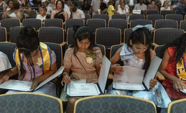 Sophia Prado, center, looks at her diploma during a graduation ceremony at Trevor Day School, Friday, June 21, 2024 in New York. Thousands of migrant families in New York City are facing a summer of uncertainty for their school-aged children with a citywide limit of 60 days in a shelter before needing to reapply or find their own. (AP Photo/Jeenah Moon)