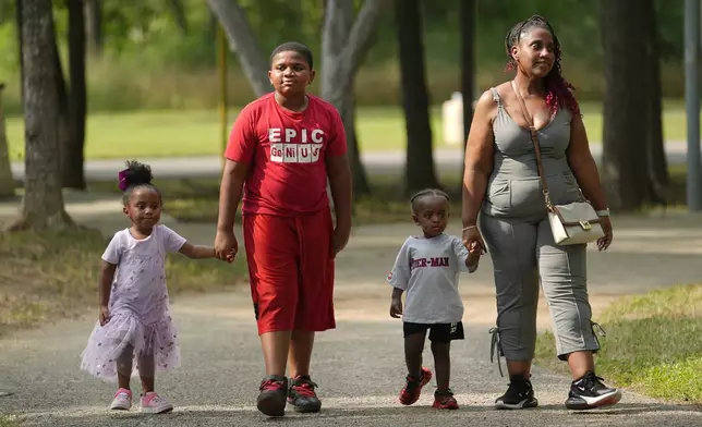 Tamika Davis, right, walks through MLK Park with three of her children, from left, Shanara, 3, Matthew, 11, and Lionel Jr., 2, in San Antonio, Thursday, May 30, 2024. As a cancer patient, she said a case manager set a book of available resources on her bedside table and did nothing else. Davis, a nursing professor, found the book confusing. (AP Photo/Eric Gay)