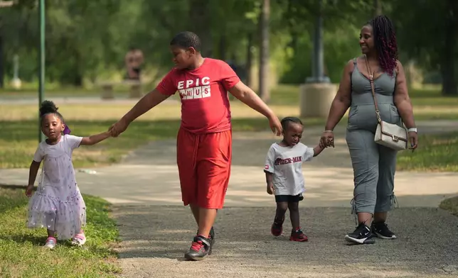 Tamika Davis, right, walks through MLK Park with three of her children, from left, Shanara, 3, Matthew, 11, and Lionel Jr., 2, in San Antonio, Thursday, May 30, 2024. Davis said friends and family watched her kids for most of her doctor visits during treatment last year for colon cancer. But she couldn't afford additional childcare, and she didn't know where to look for assistance. (AP Photo/Eric Gay)