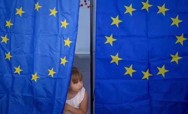 A child peers from a voting cabin during European and local elections in Baleni, Romania, Sunday, June 9, 2024. Voters across the European Union are going to the polls on the final day of voting for the European parliamentary elections to choose their representatives for the next five-year term. (AP Photo/Andreea Alexandru)