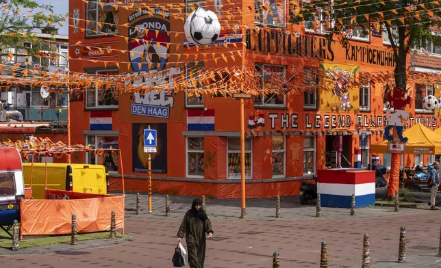 A women walks past inflatable soccer balls, orange tarp, orange bunting, and Dutch national flags as she walks along Marktweg street in The Hague, Netherlands, Thursday June 13, 2024, one day ahead of the start of the Euro 2024 Soccer Championship. The Marktweg is one of several streets in the Netherlands that get an all-encompassing orange facelift during European Championships and World Cups when the national team, known as Oranje after the Dutch royal family and the color of their shirts, are playing. (AP Photo/Peter Dejong)