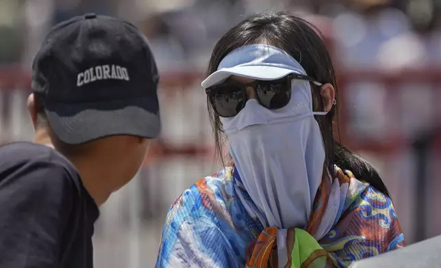 A woman wearing a face cover chats with a man as they visit the Forbidden City in a hot and sunny day in Beijing, Sunday, June 9, 2024. (AP Photo/Andy Wong)