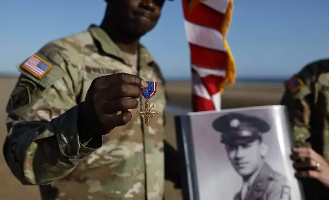 A soldier of the First U.S. Army shows the Distinguished Service Cross while another holds the portrait of of Waverly Woodson Jr., a medic who was part of the only Black combat unit to take part in the D-Day invasion of France during World War II, being posthumously awarded the Distinguished Service Cross in recognition of the heroism and determination he showed treating troops under heavy enemy fire , on Omaha Beach in Colleville-sur-Mer, France on Friday, June 7, 2024, (AP Photo/Jeremias Gonzalez)