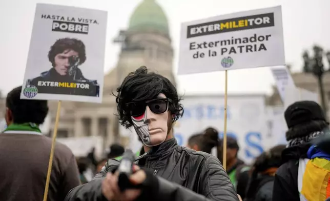 A masked anti-government protester aims a toy gun during a demonstration outside Congress where lawmakers debate a reform bill promoted by President Javier Milei in Buenos Aires, Argentina, Wednesday, June 12, 2024. The sign at right reads in Spanish "Exterminator of the homeland." (AP Photo/Natacha Pisarenko)