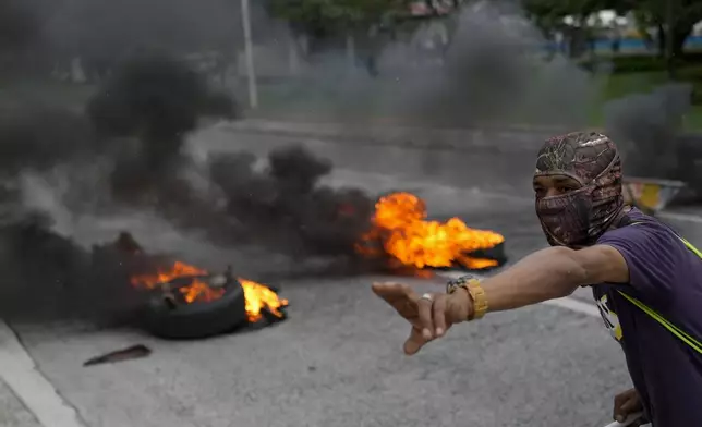 A masked protester shouts to his colleagues as they block a street with burning tires as part of the national strike by the construction union, in Panama City, June 20, 2024. (AP Photo/Matias Delacroix)