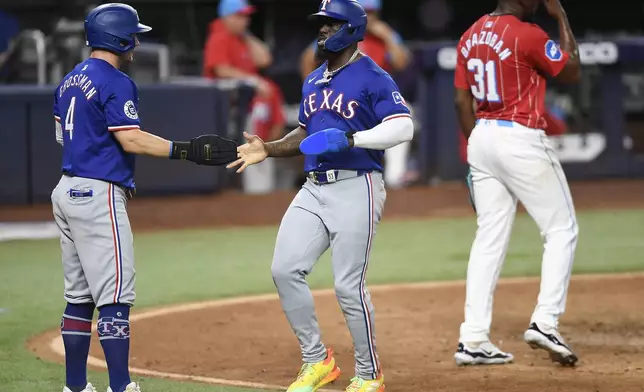 Texas Rangers' Adolis García, center, and Robbie Grossman (4) react after scoring against the Miami Marlins during the ninth inning of a baseball game, Saturday, June 1, 2024, in Miami. (AP Photo/Michael Laughlin)